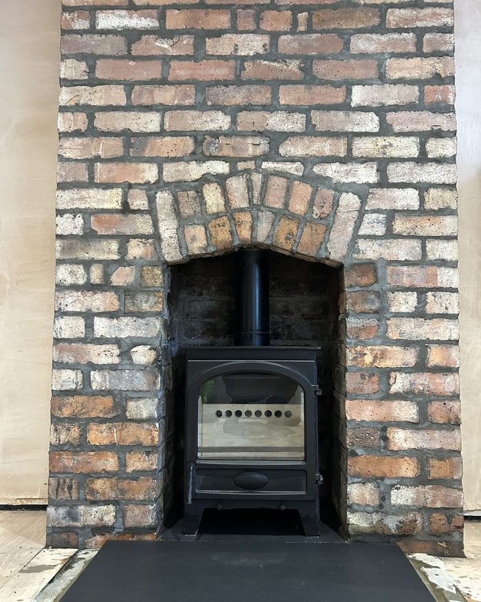 A stove set into a reclaimed brick surround with an arched brick lintel and slate hearth