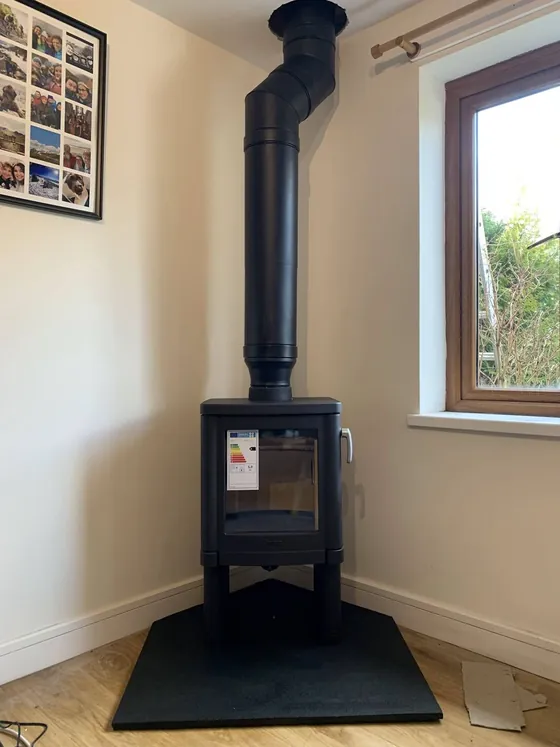 Wood burner set into a brick chimney breast with a herringbone hearth, flames lit