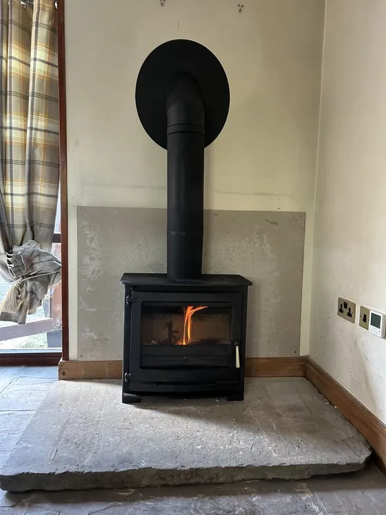 Multi-fuel stove under a curved brick archway with a patterned tiled hearth, lit