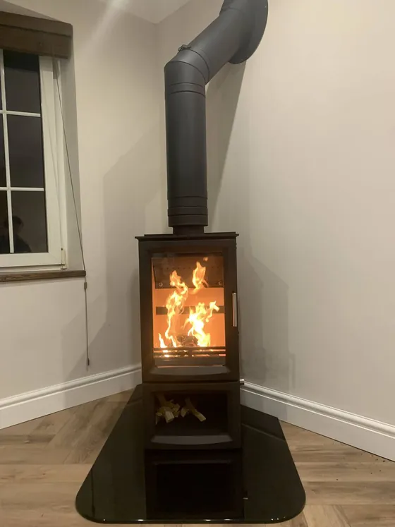 Corner wood burner on a curved glass hearth plate with a lit fire
