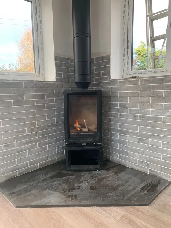 Corner stove against a grey brick chimney breast, lit