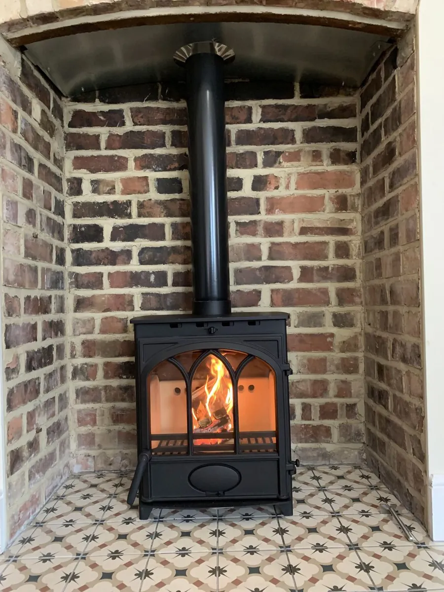 A multi-fuel stove installed under a curved brick archway on a patterned tiled hearth, fire lit