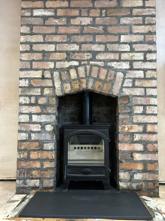 Inset stove framed by a reclaimed brick surround with a brick arch lintel
