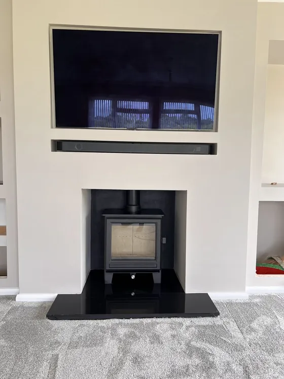Freestanding stove on a black granite hearth below a recessed TV, finished install