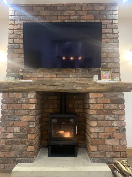 Inset stove in a brick chimney breast with a wall-mounted TV above