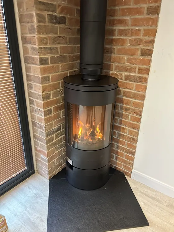 Cylindrical wood burner in a brick corner recess with the fire lit
